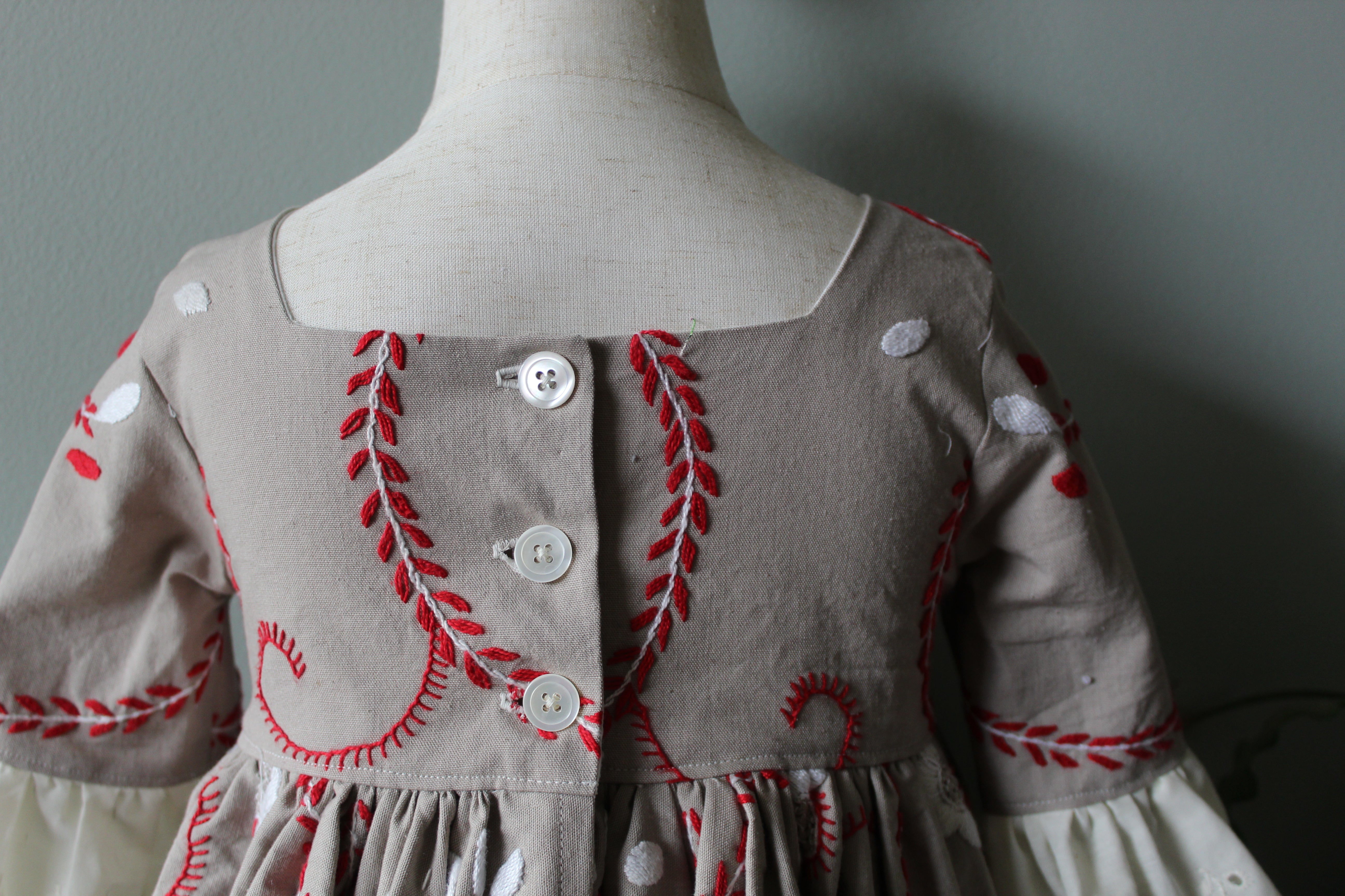 Children's dress with red embroidery on a mannequin against a gray background