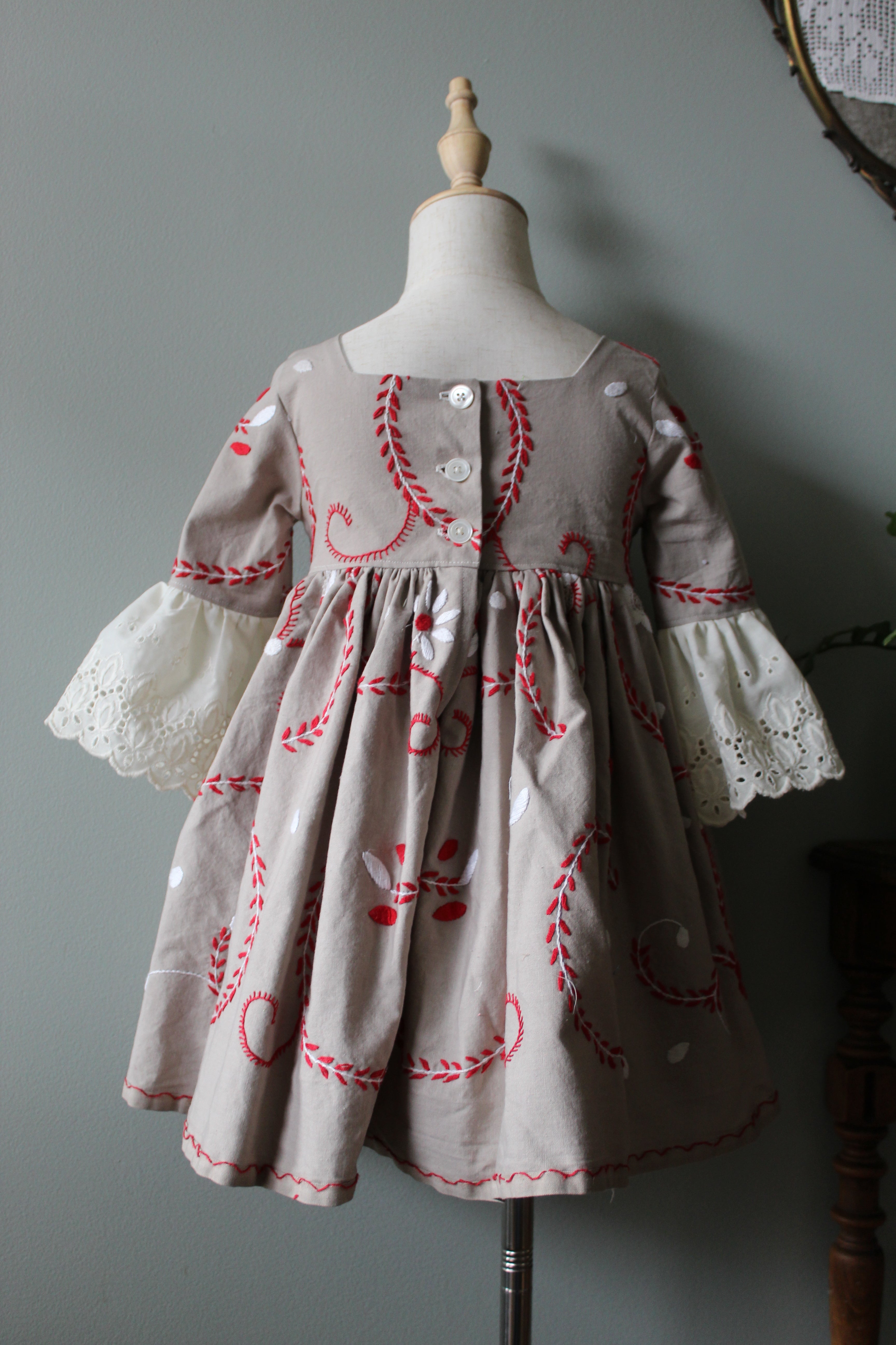 Small dress with red embroidery on a mannequin against a gray background