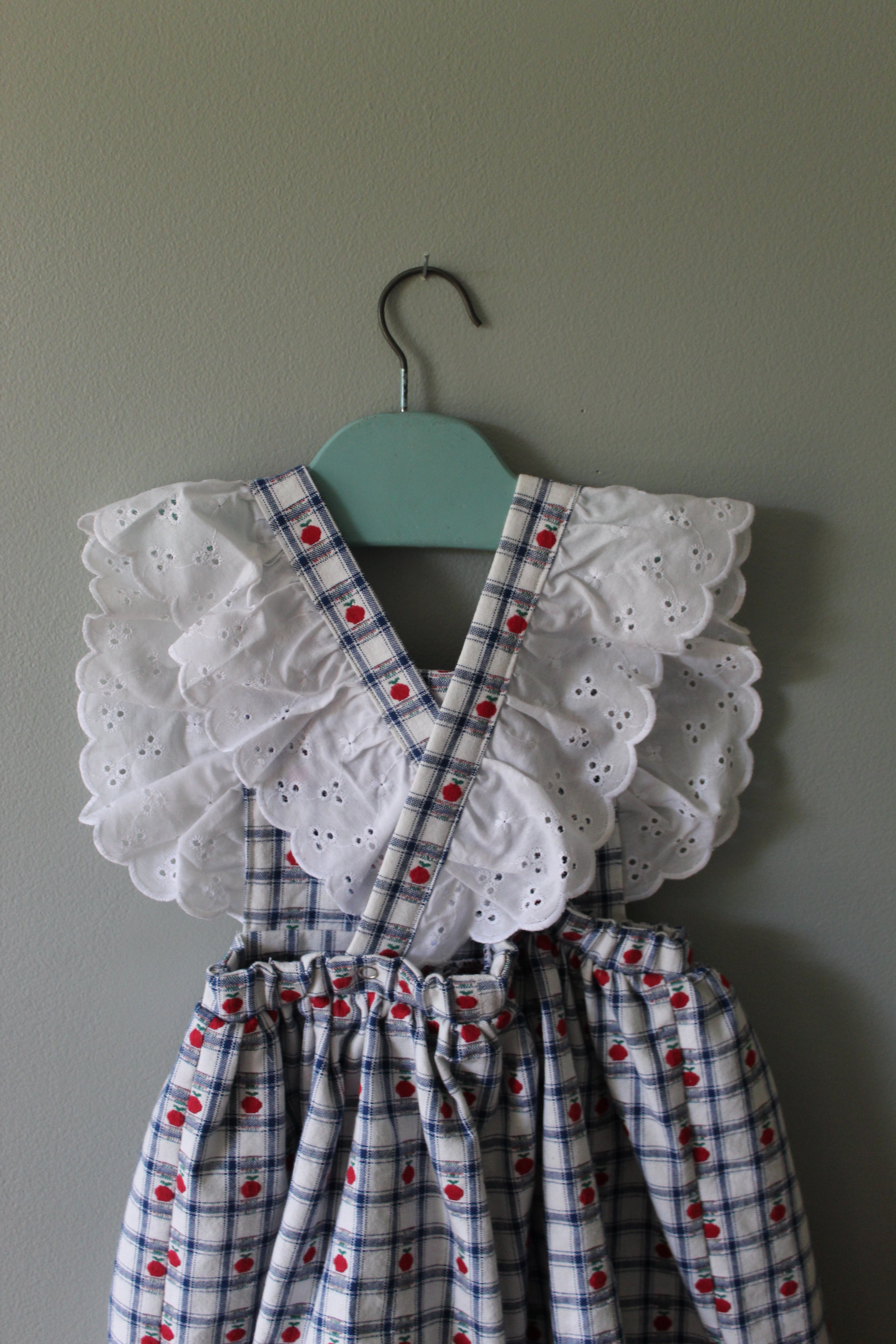 Dress with white lace details and red polka dots on a hanger against a gray background