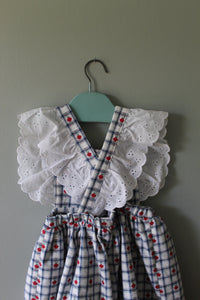 Dress with white lace details and red polka dots on a hanger against a gray background