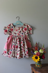 Floral-patterned girls tunic on a hanger with a small bouquet of flowers on a gray surface.