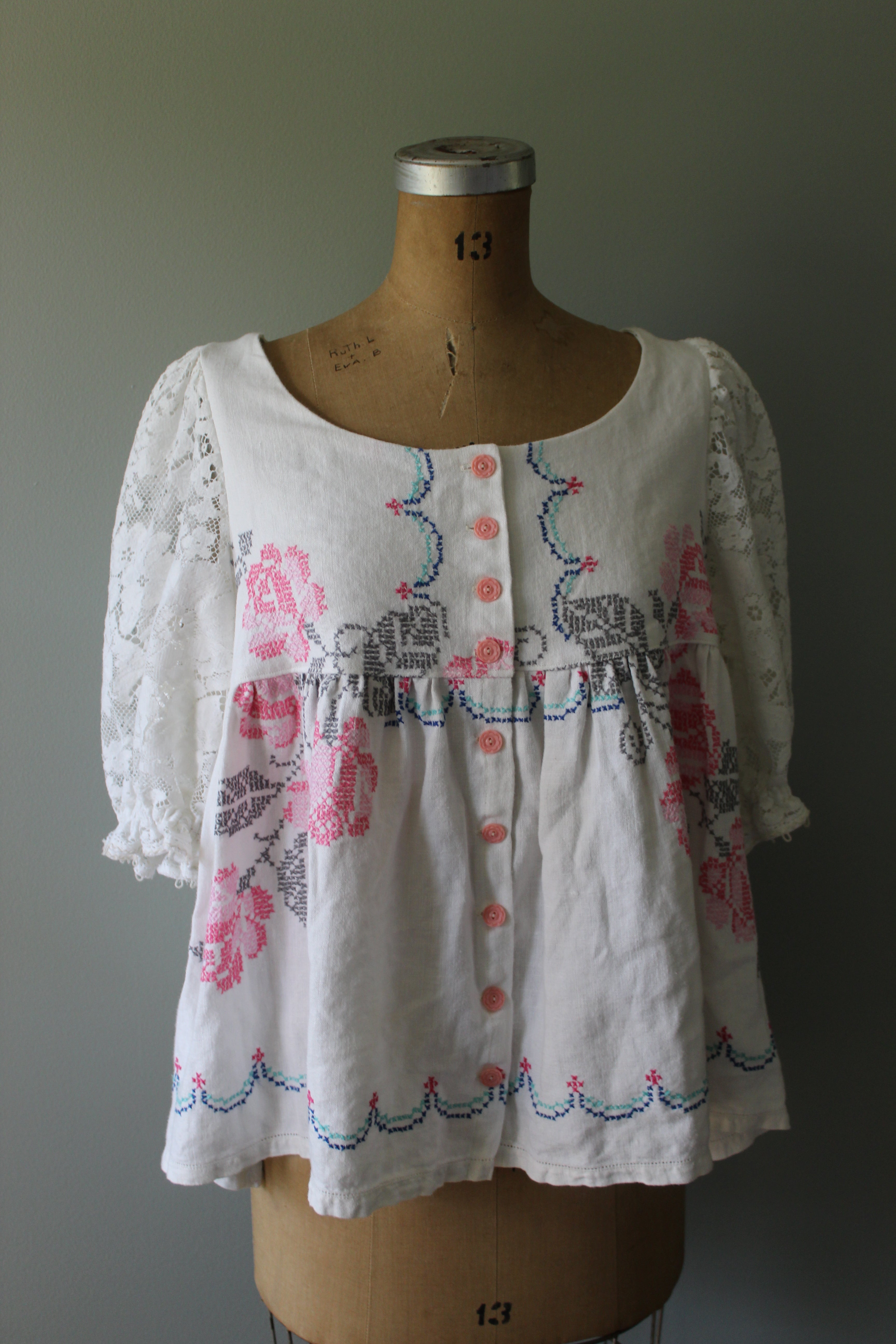 White top with floral embroidery on a mannequin against a gray background