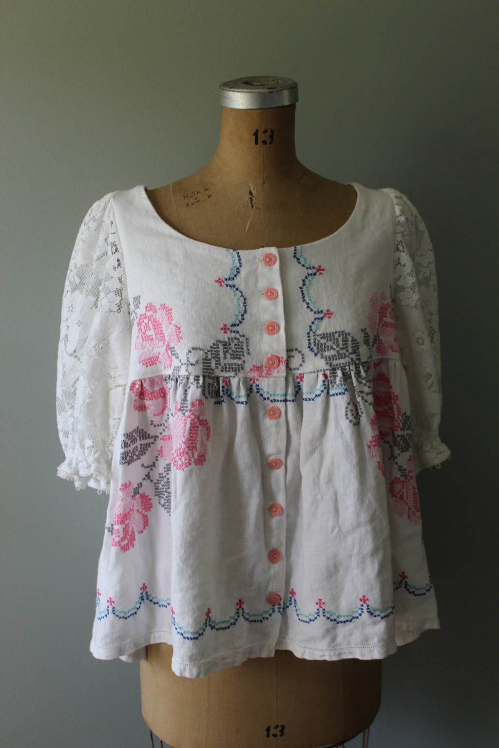 White top with floral embroidery on a mannequin against a gray background