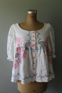 White top with floral embroidery on a mannequin against a gray background