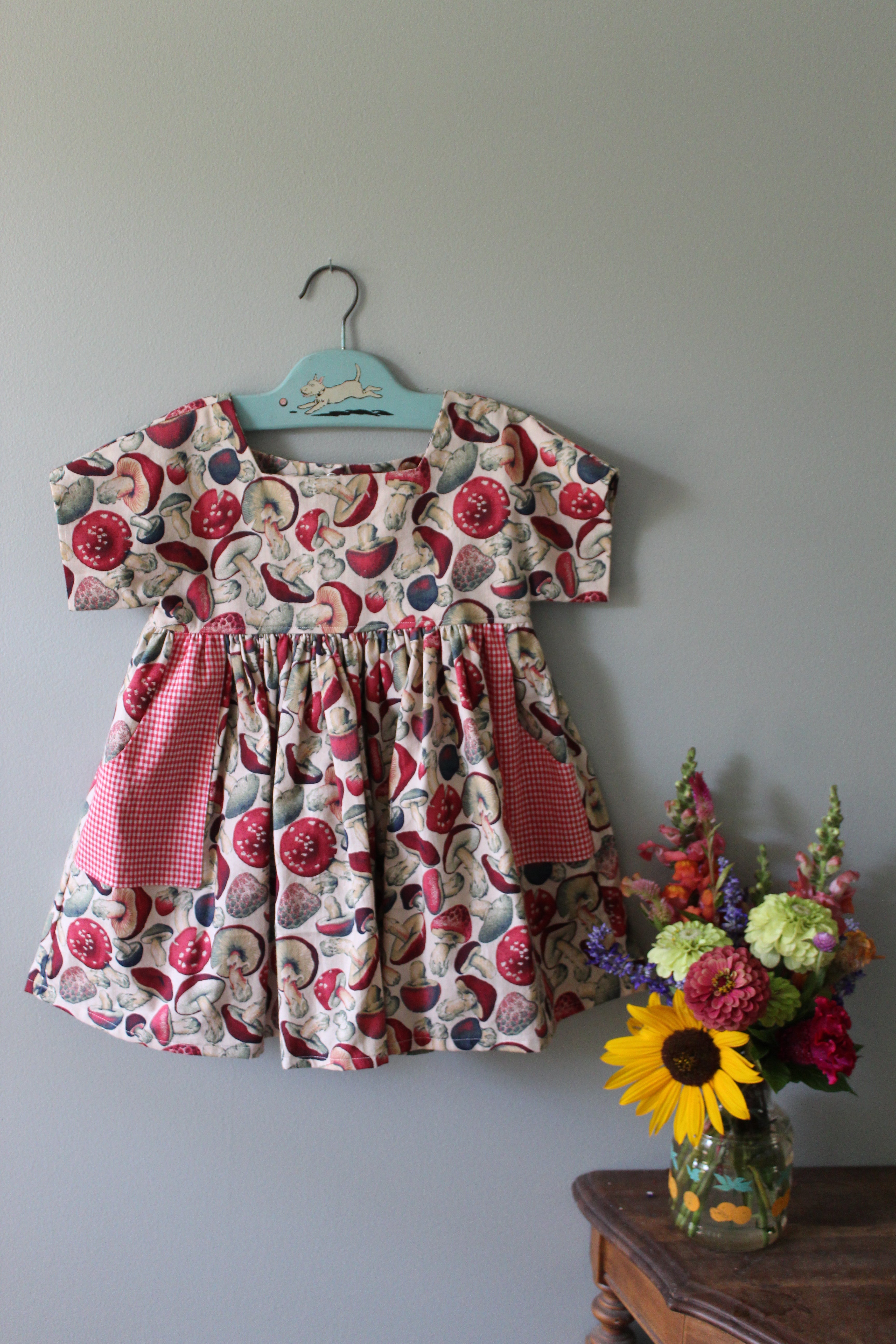Floral-patterned girls tunic on a hanger with a bouquet of flowers on a gray surface