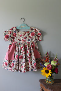 Floral-patterned girls tunic on a hanger with a bouquet of flowers on a gray surface