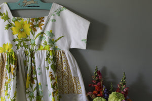 Floral dress with a plain white top on a hanger against a gray wall with flowers below.