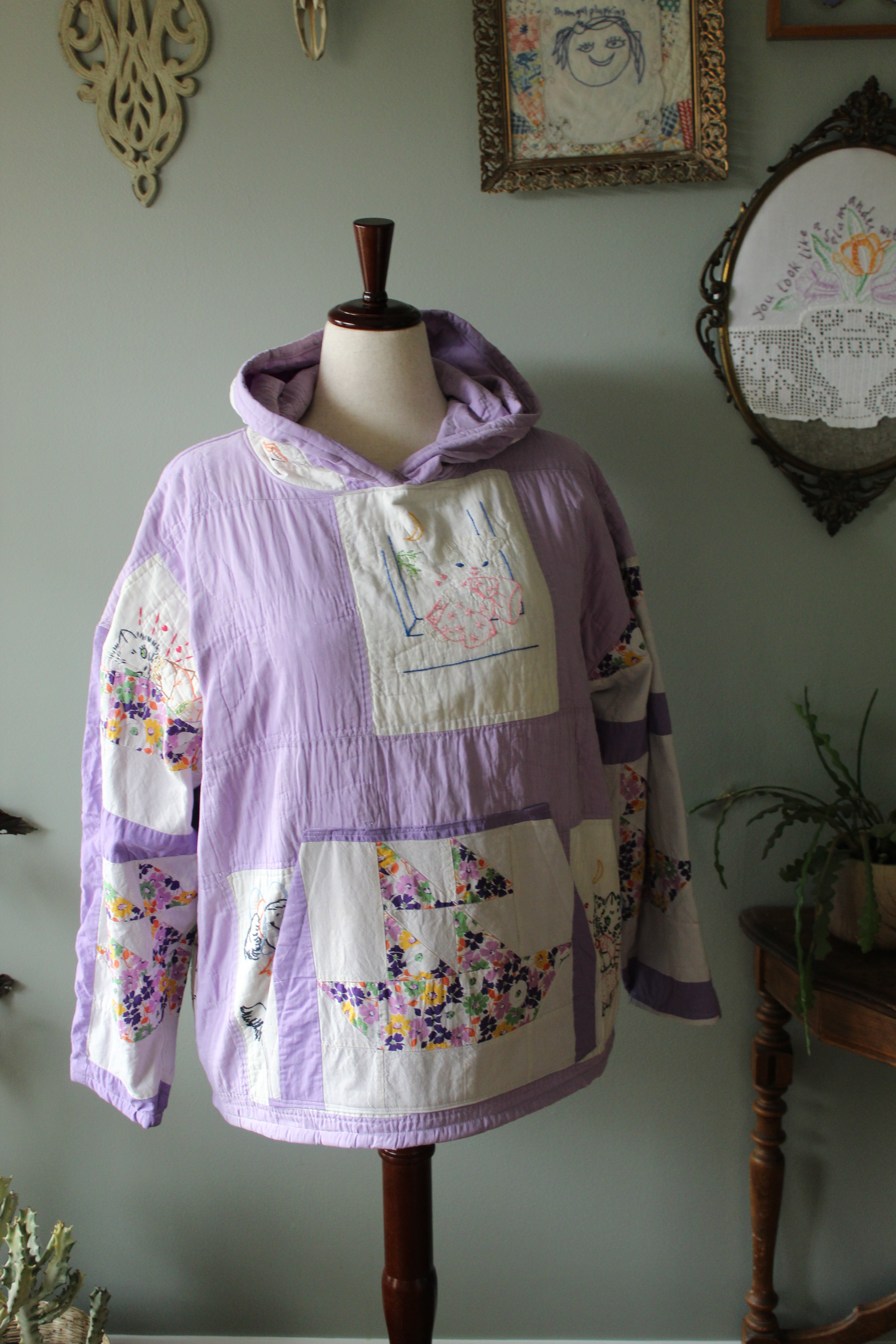 Purple quilt hoodie with floral patterns on a wooden stand against a light green wall.