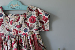 Children's dress with mushroom pattern on a hanger against a plain wall