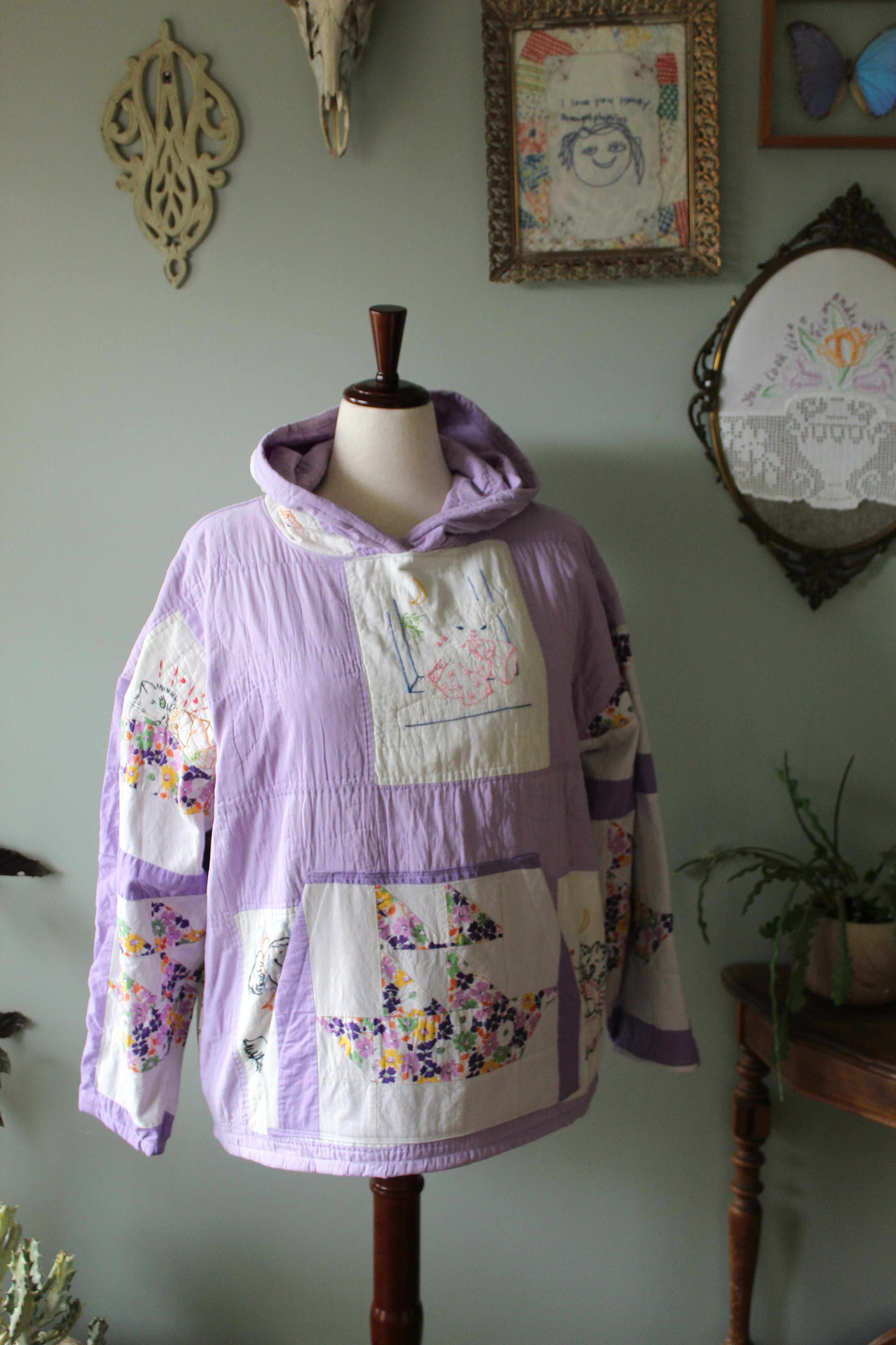 Patchwork quilt hoodie on a wooden frame against a light green wall with decorative elements.