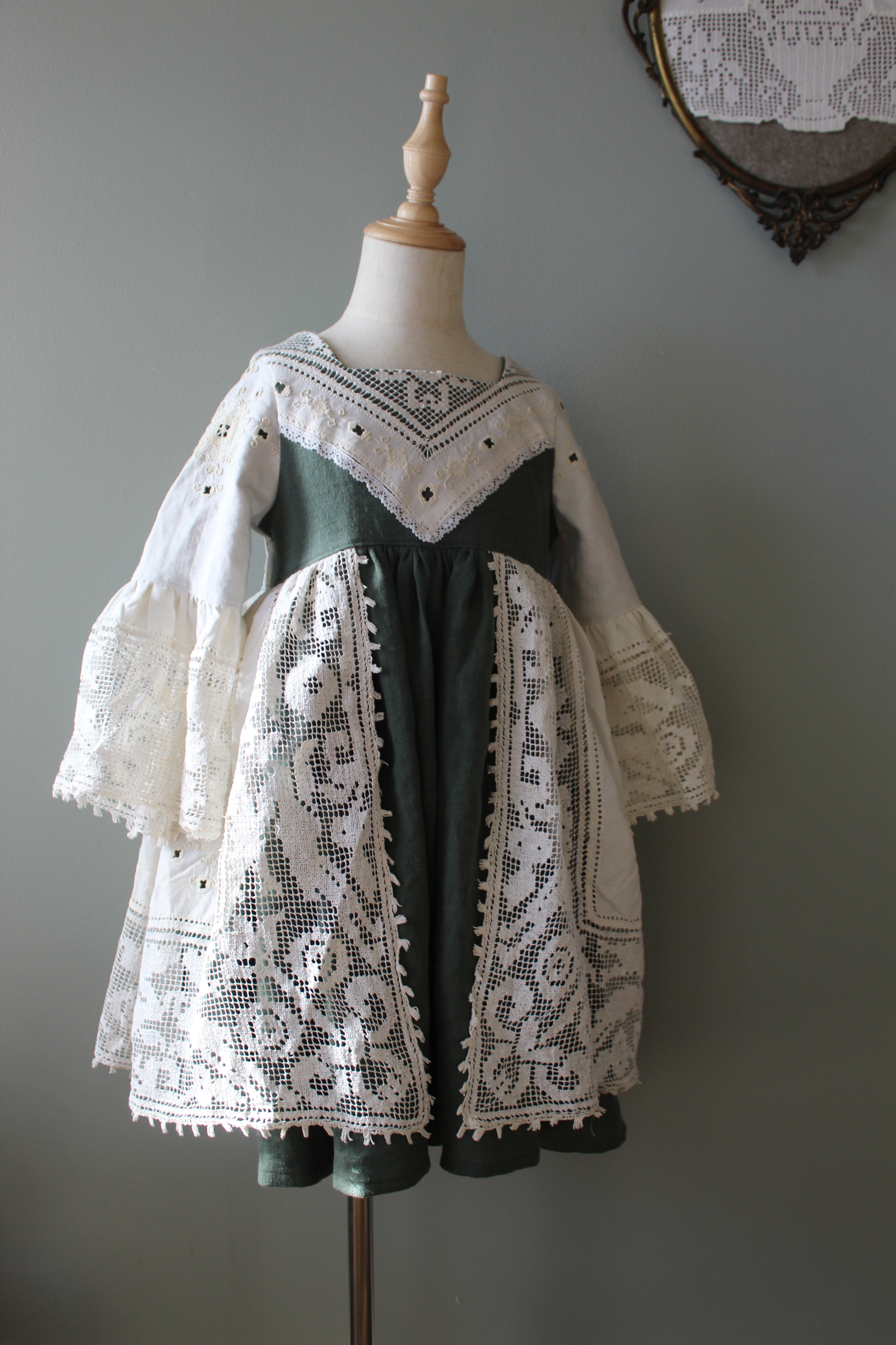 Mannequin wearing a green dress with white lace details on a gray background