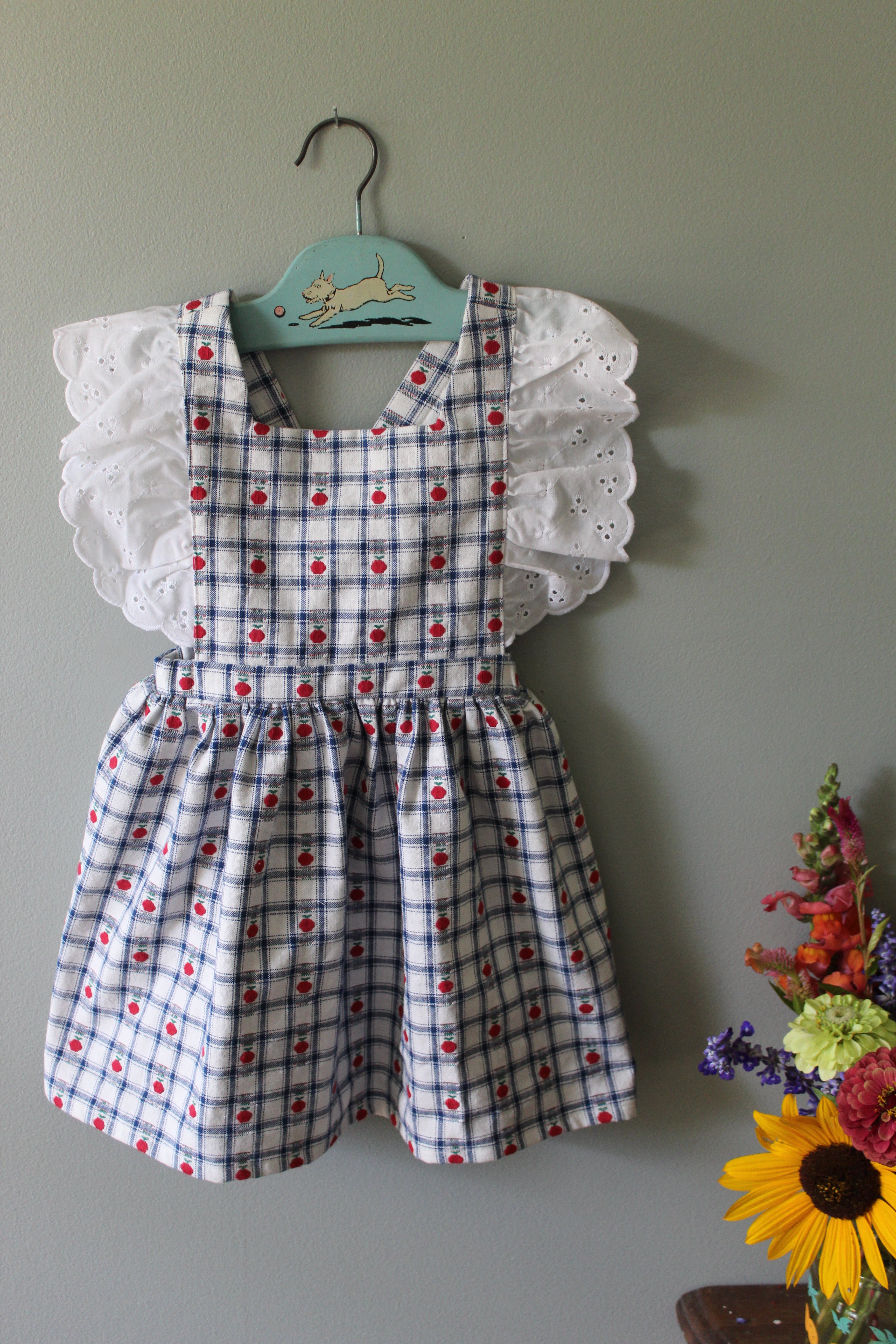 Children's dress with checkered pattern and white lace details on a gray background