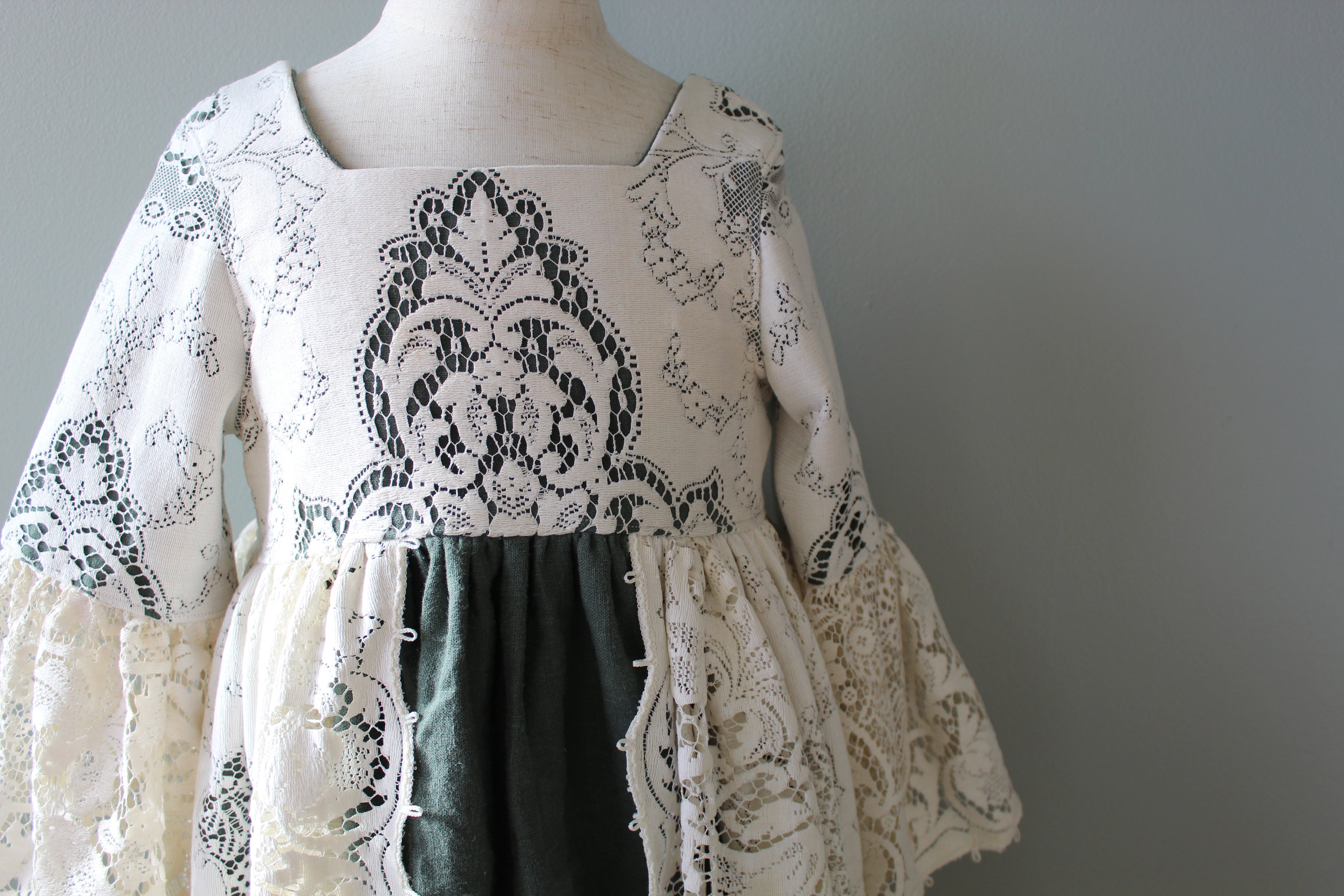 Mannequin wearing a white lace top with black embroidery on a gray background