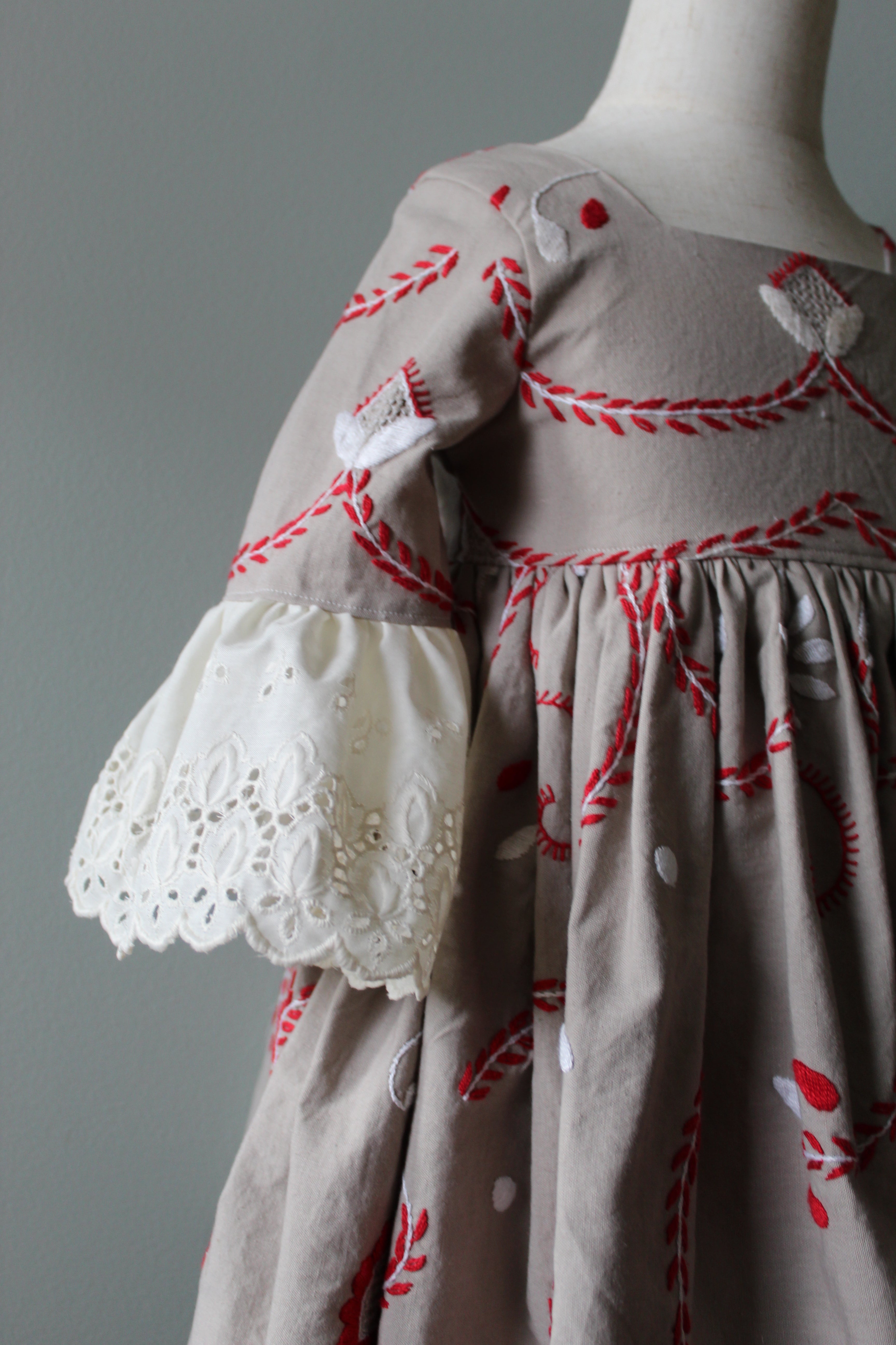 Close-up of a dress with red embroidery and white lace details on a gray background