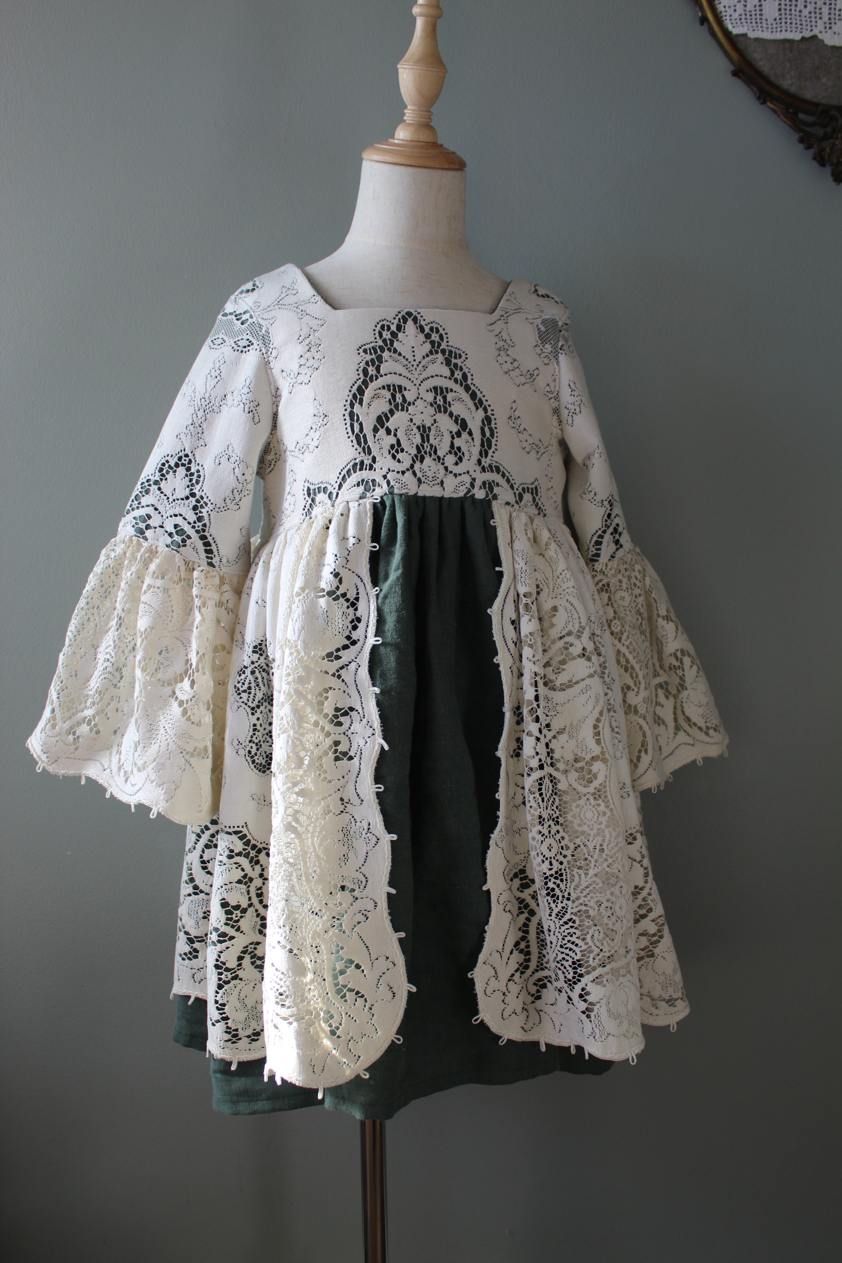 Mannequin wearing a green dress with white lace overlay against a gray background