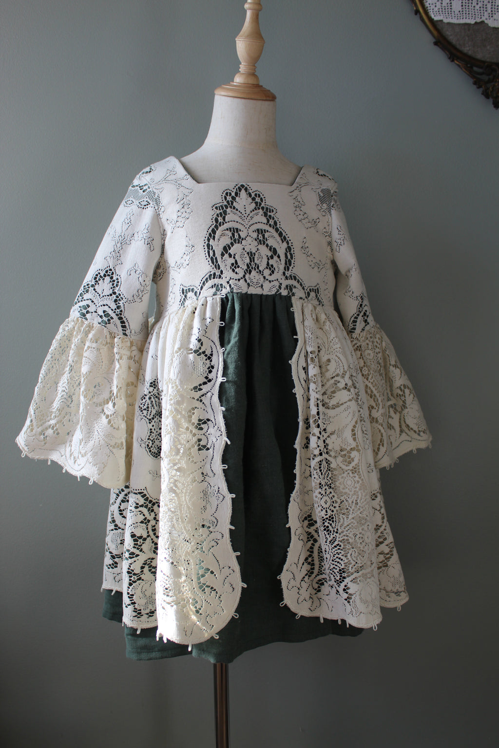 Mannequin wearing a green dress with white lace overlay against a gray background