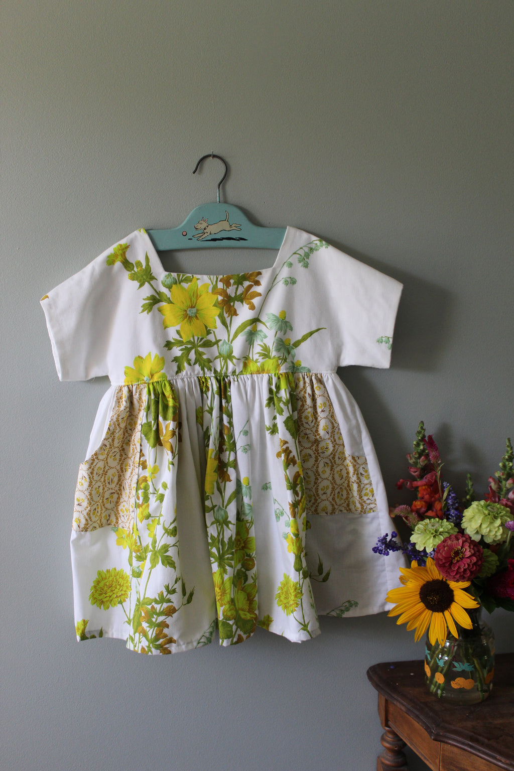 Floral-patterned shirt on a hanger against a gray background with a vase of flowers.
