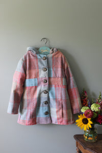 Pink plaid jacket on a hanger against a light green wall with flowers in the foreground.