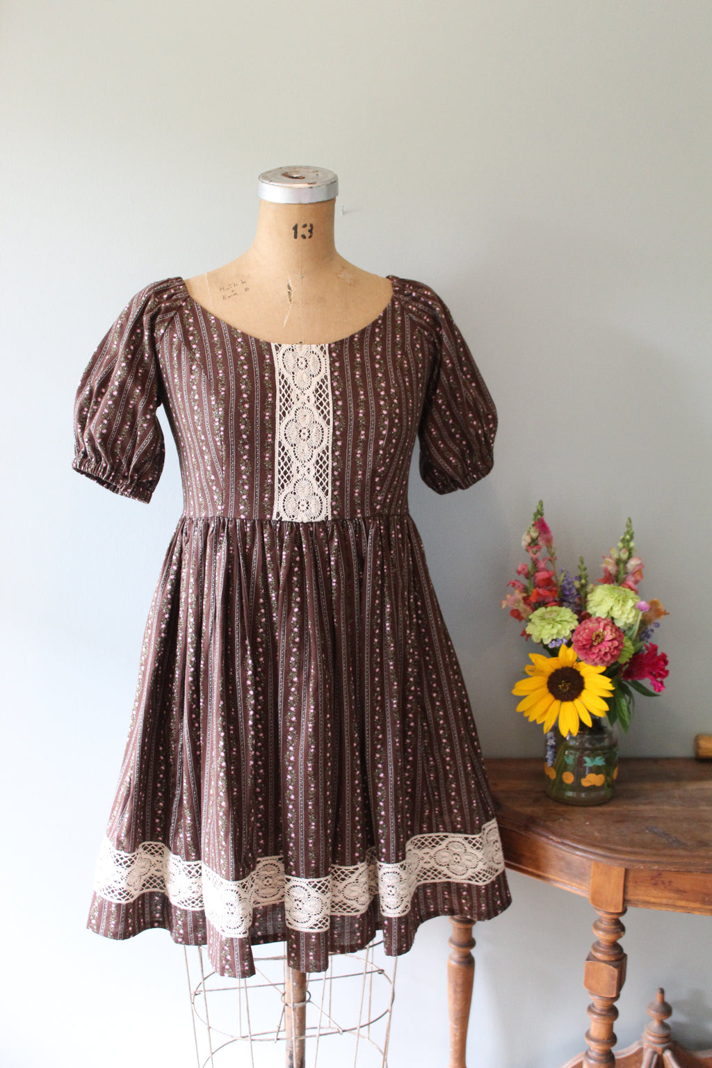 Mannequin wearing a brown dress with lace details on a light gray background
