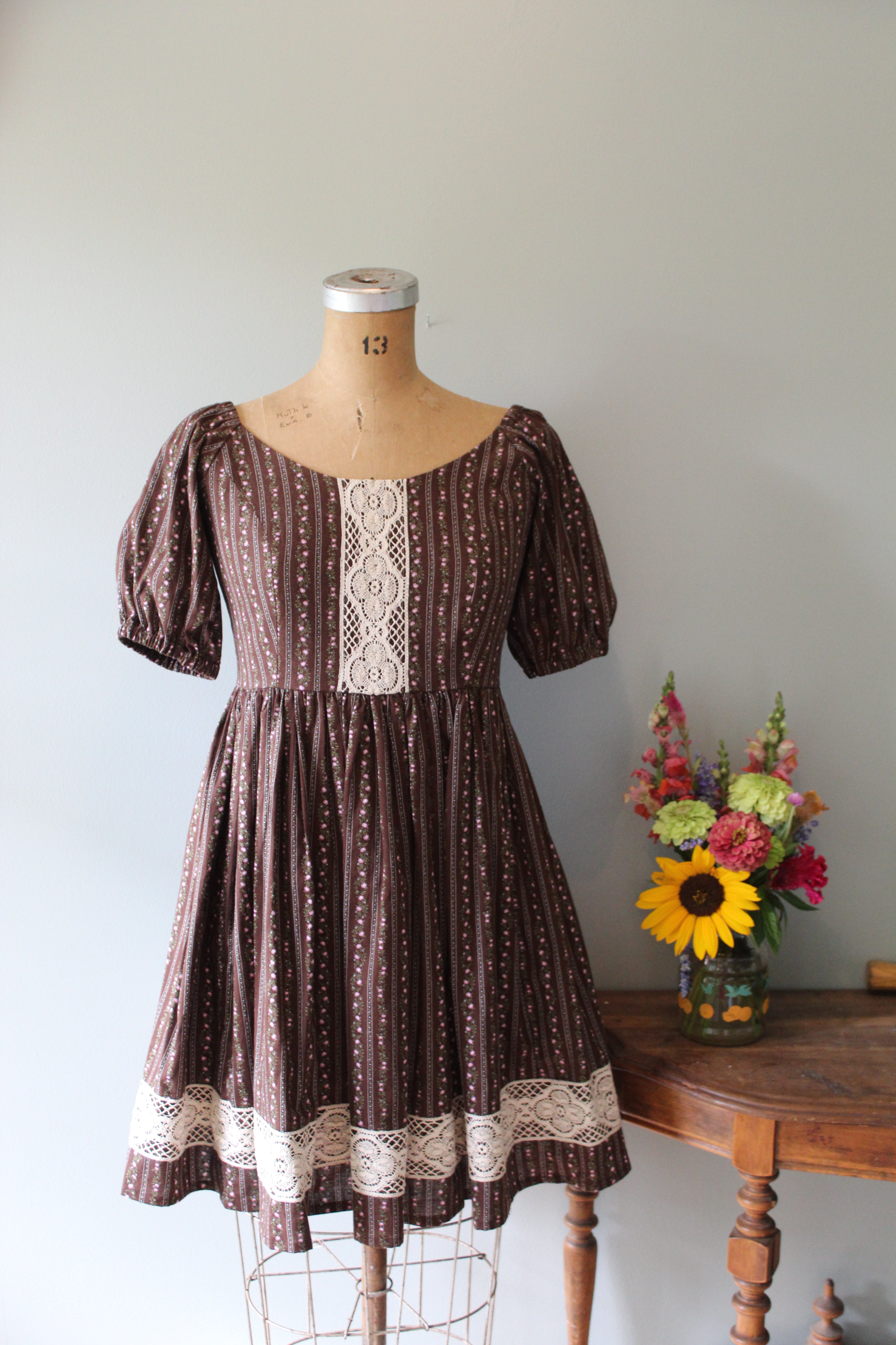 Mannequin wearing a brown dress with lace details against a plain background