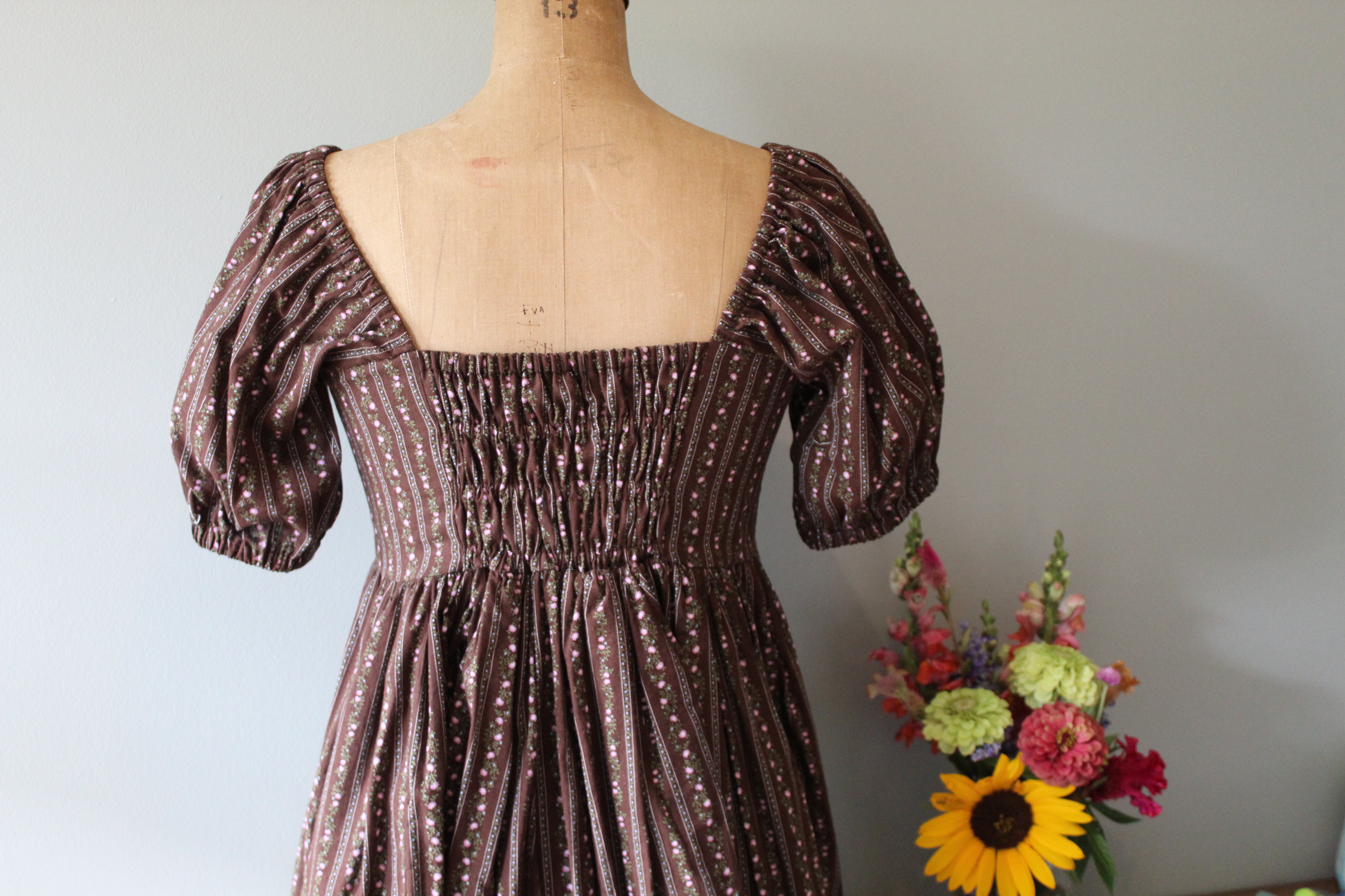 Brown patterned dress on a mannequin with a bouquet of flowers against a plain background