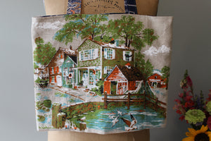 Tote bag with a printed design of a village scene held by a person.