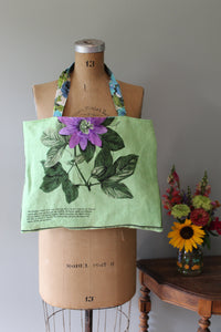 Green fabric tote bag with floral design draped over a mannequin bust against a neutral background