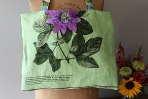 Green tote bag with floral design held by a person, with a blurred background