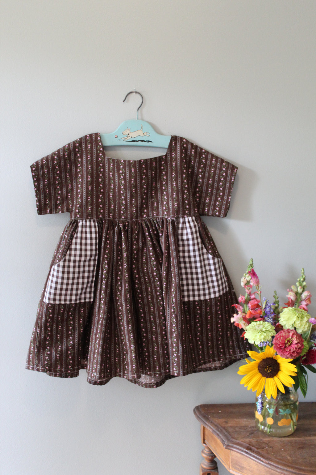 Brown patterned tunic on a white surface with flowers and a wooden chair.