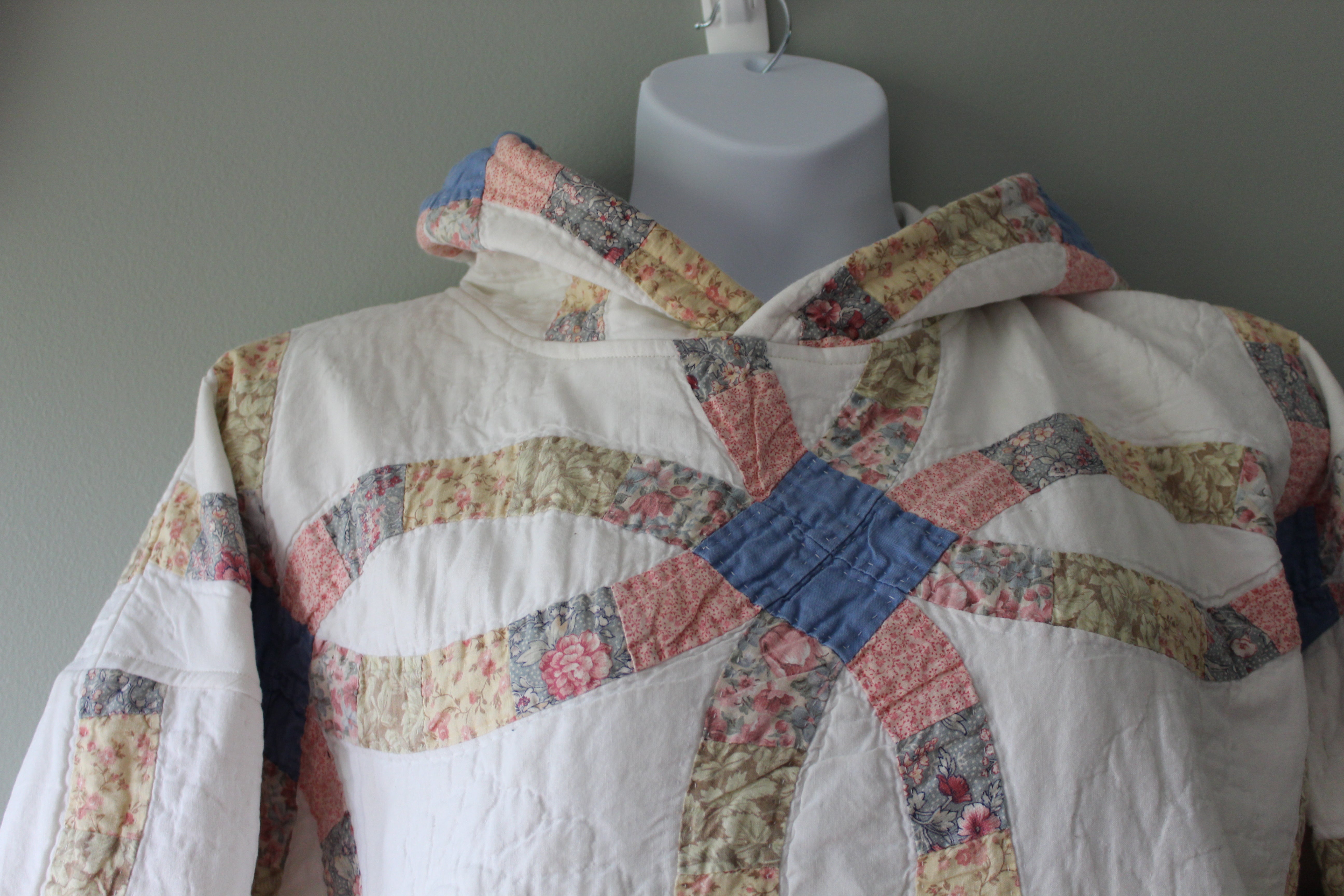 Quilted garment with floral patterns on a mannequin against a gray background