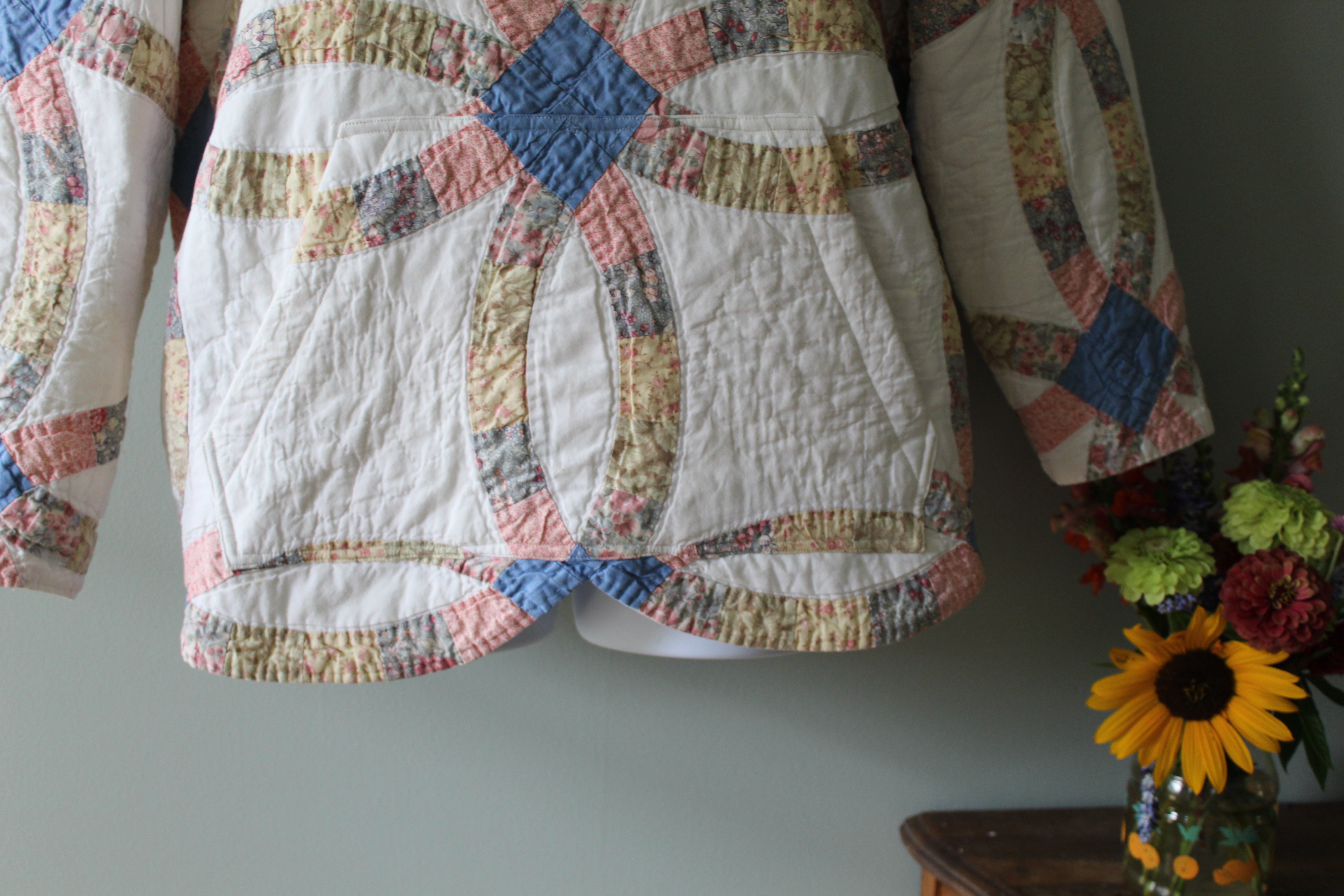 Quilt with a colorful pattern hanging on a wall next to a vase with flowers.