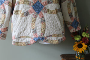 Quilt with a colorful pattern hanging on a wall next to a vase with flowers.