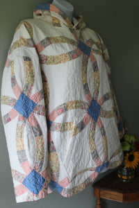 Quilt hoodie with a circular pattern draped over a surface against a gray wall.