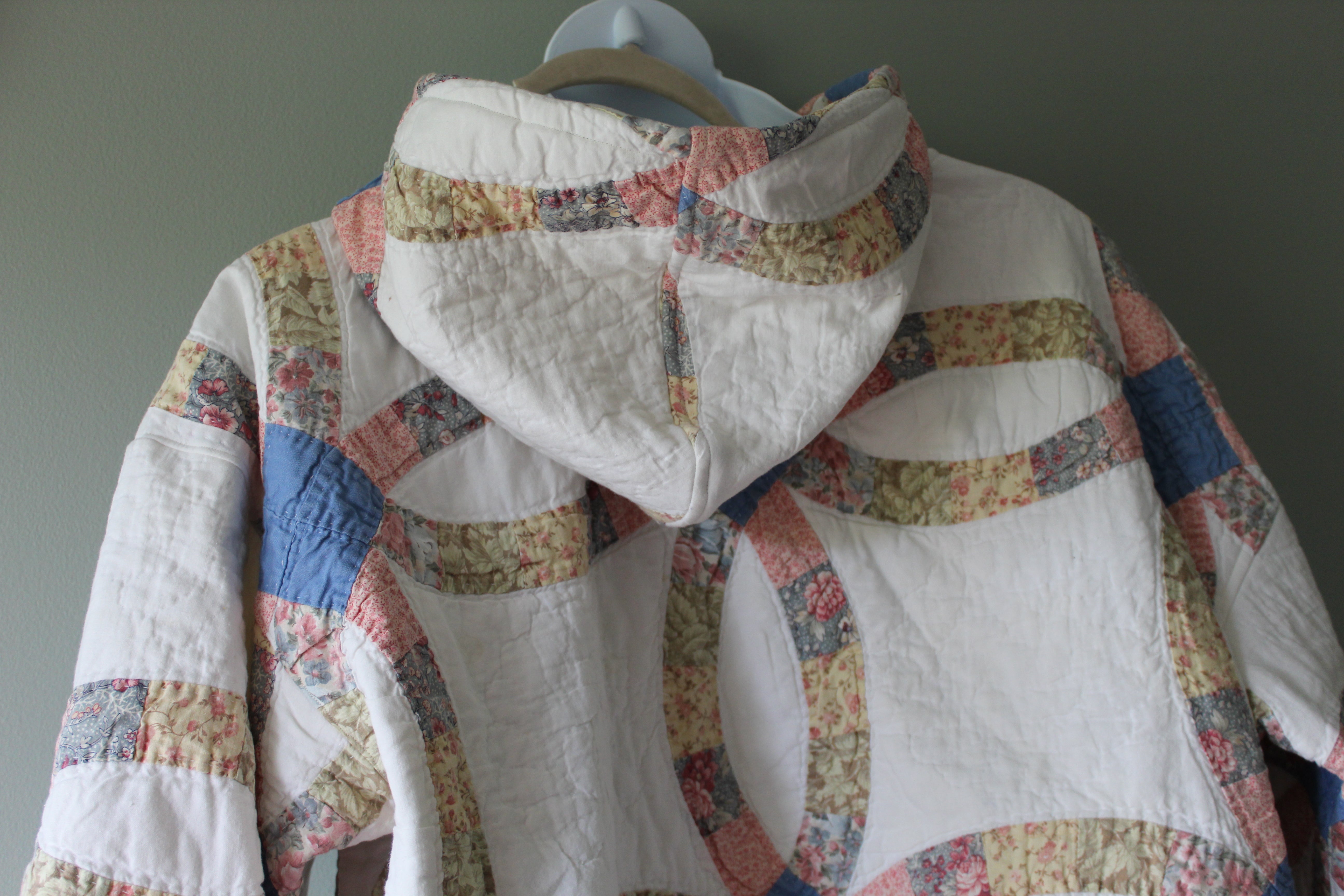 Patchwork quilt hoodie on a hanger against a plain background