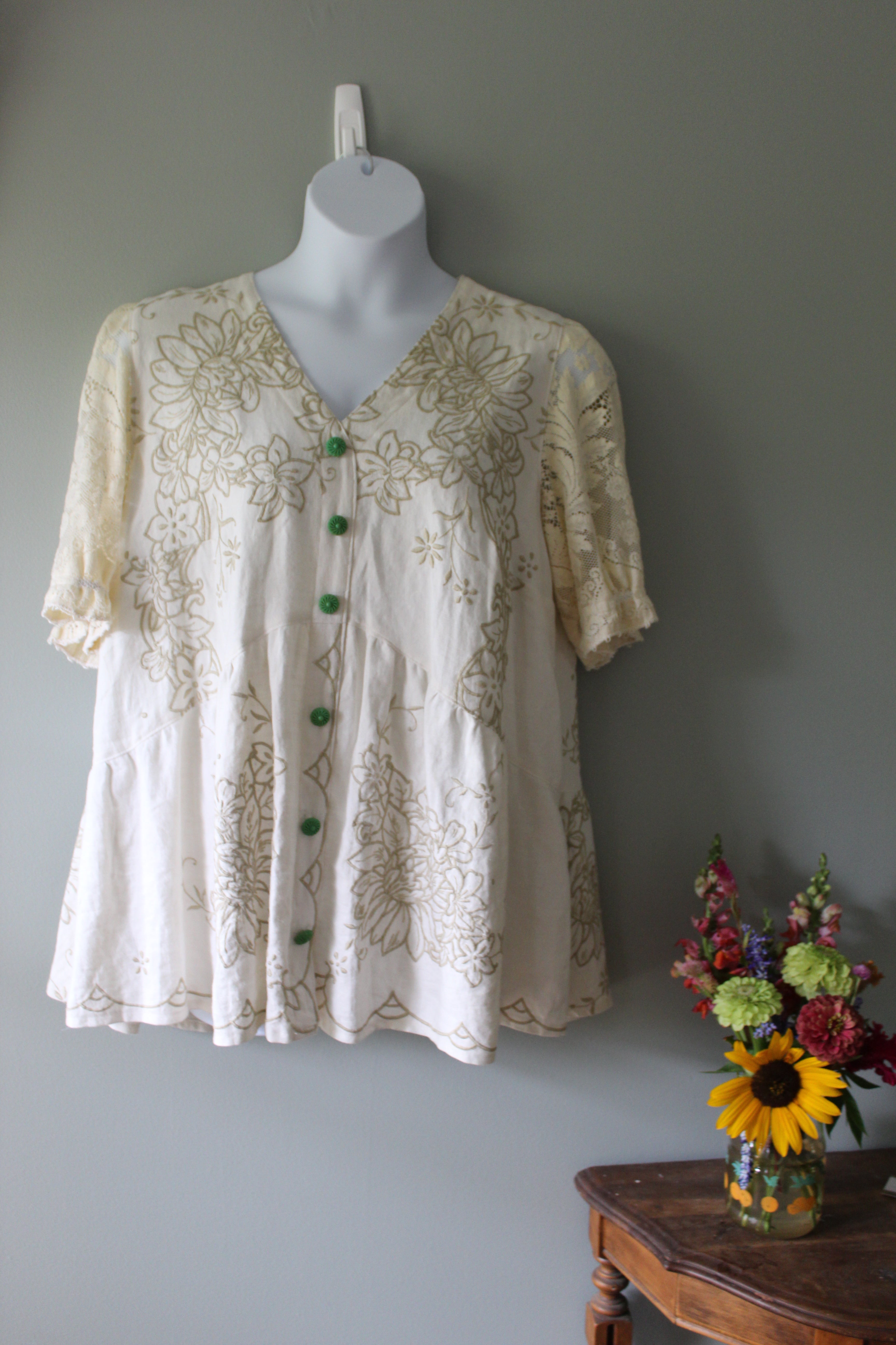 White lace top on a mannequin against a gray wall with flowers in the foreground.