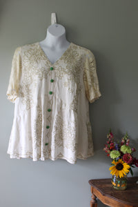 White lace top on a mannequin against a gray wall with flowers in the foreground.