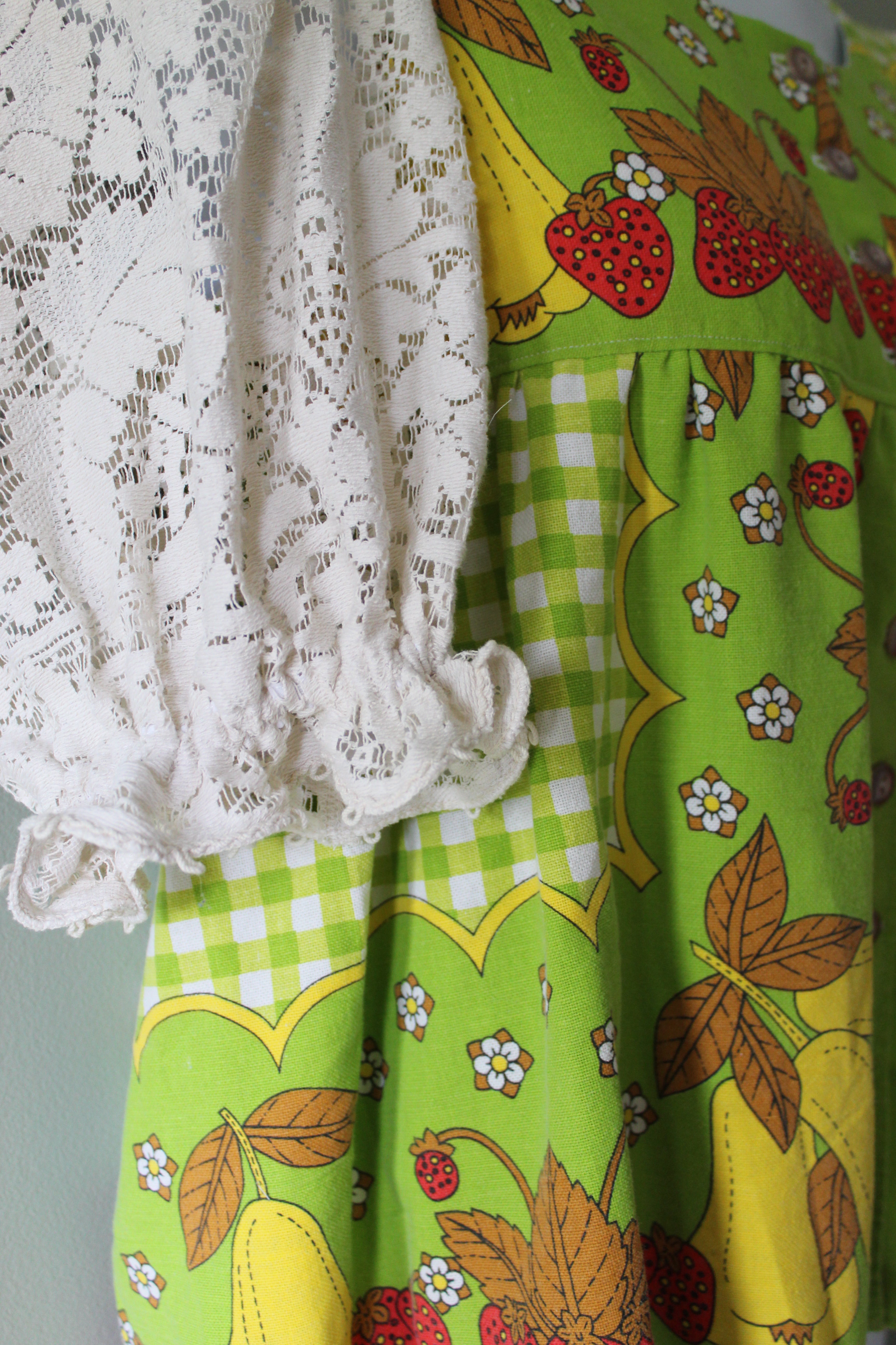 Green fabric blouse with strawberry patterns and a white lace sleeves.