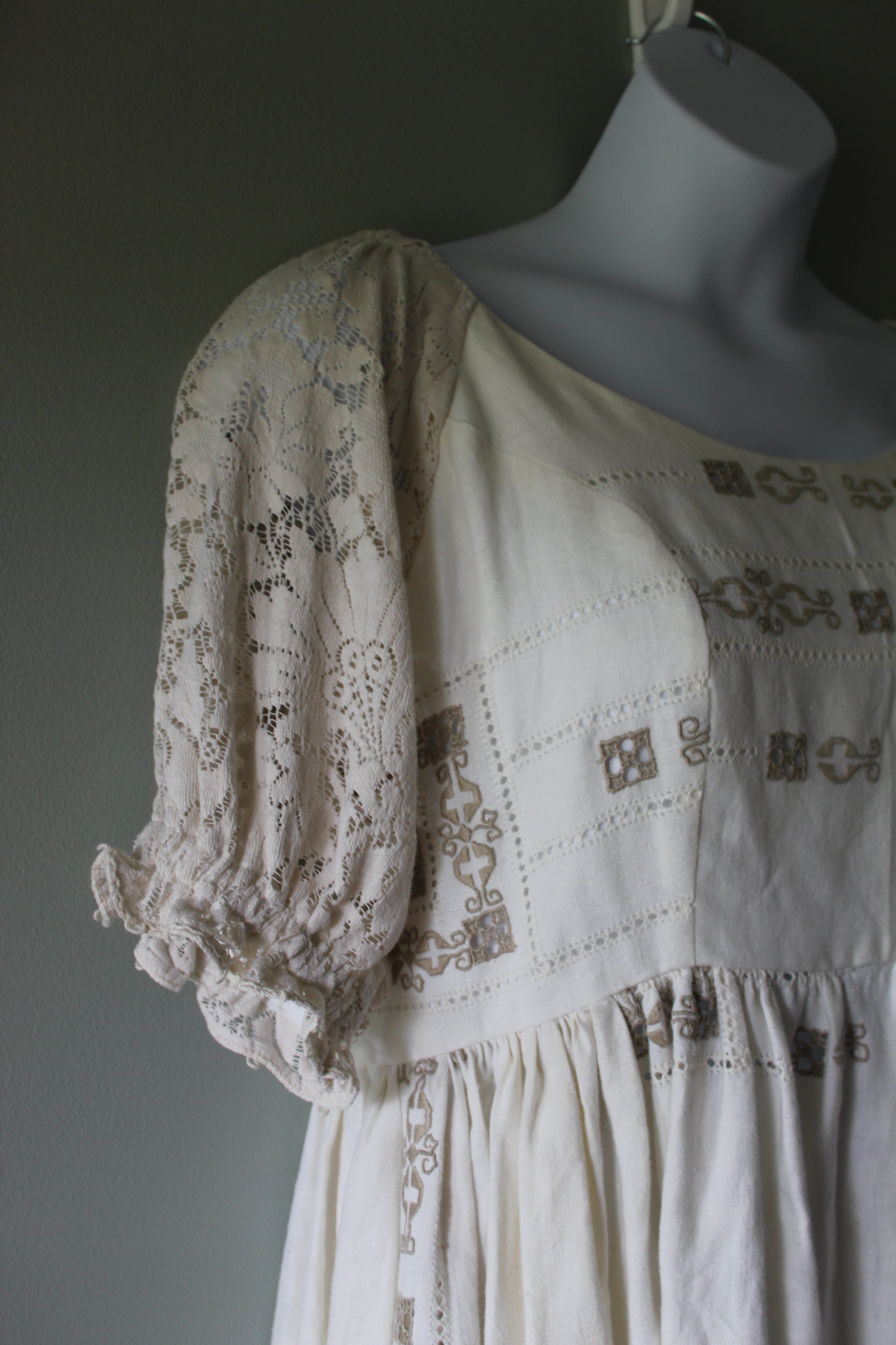 White dress with intricate lace and embroidery on a mannequin against a gray background