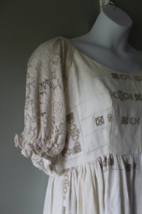 White dress with intricate lace and embroidery on a mannequin against a gray background