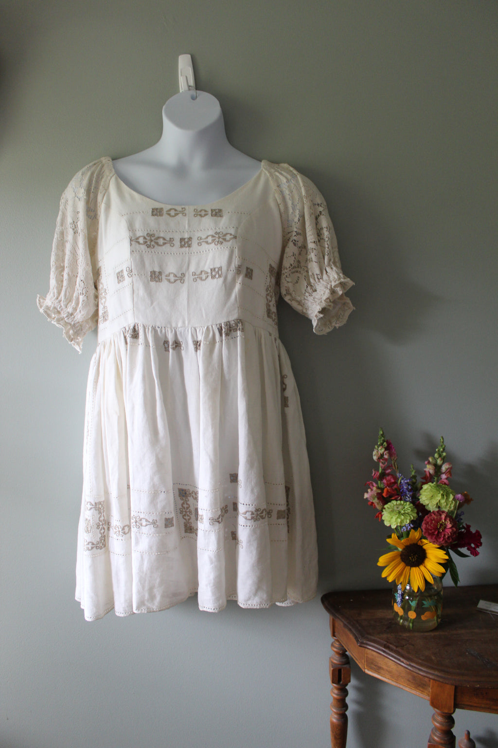 White lace dress on a mannequin with a bouquet of flowers on a gray background